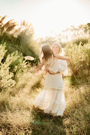 Mother and child twirling together in white dresses during golden hour.