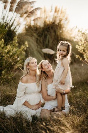 Beautiful outdoor family portrait during sunset with matching white dresses in tall grass.