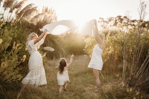Family plays and dances together in a field at sunset surrounded by tall pampas grass.