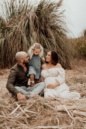 Intimate family moment photographed in a natural setting with dried grass and soft lighting.