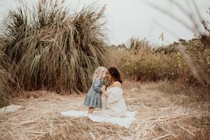 Tender moment between mother and child sitting on blanket among tall grass in outdoor setting.