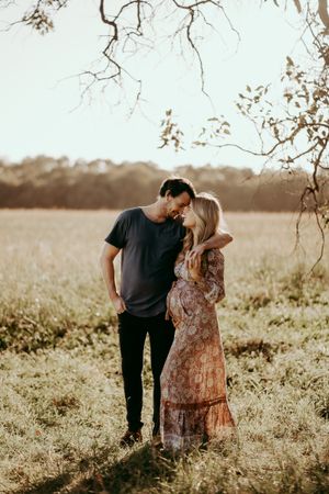 Romantic couple shares intimate moment under tree branches in sunlit field.