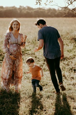 Family walks together in sunny field during maternity photo session at golden hour.