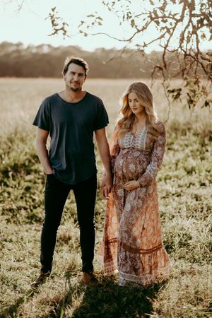Expecting couple poses in field during sunset maternity photo session.