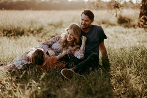 Family relaxes together in golden field during sunset portrait session.