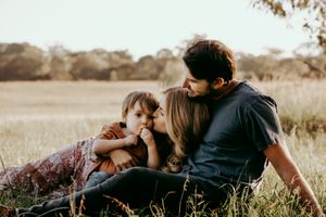 Family shares intimate moment while sitting together in sunlit field during portrait session.