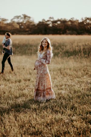 Woman in a floral dress twirls joyfully in a sunlit meadow during golden hour.