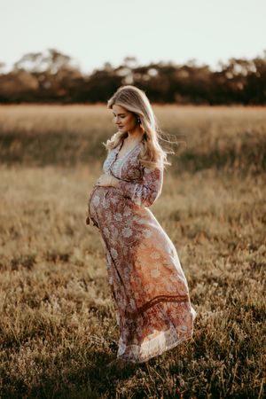 Woman in flowing dress spins gracefully through tall grass at sunset.