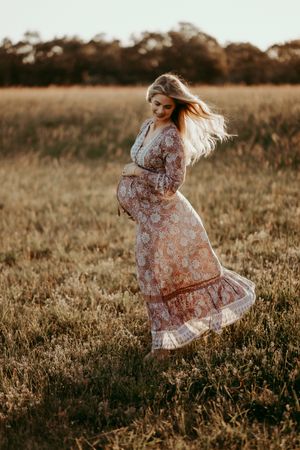 Woman dancing in a floral dress as sunlight filters through the grass.