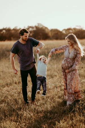 Family playing and walking together through a golden meadow at sunset.