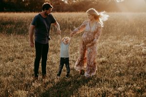 A sunset family photoshoot in a golden meadow with a toddler learning to walk between parents.