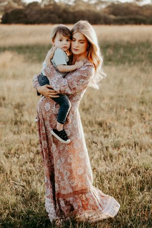 A flowing floral dress embraces two figures in a warm autumn field at sunset.