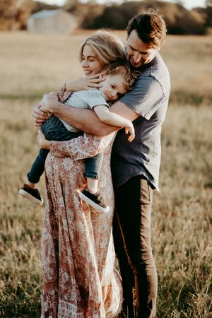 A tender family embrace captured in a golden field at sunset.