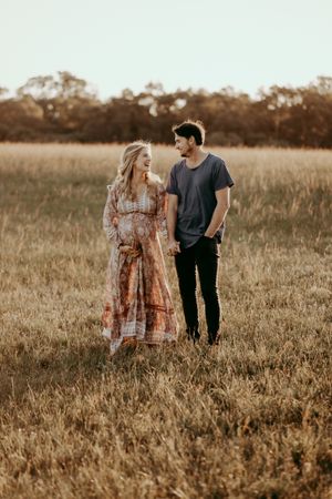 A couple shares a lighthearted moment while standing in a sun-drenched field.