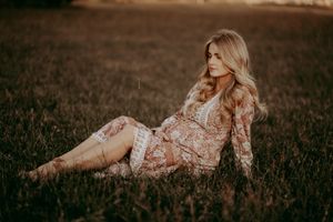 A maternity photo shoot in tall grass during golden hour featuring a floral dress.