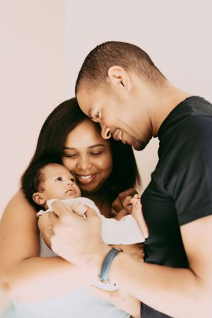 An intimate family portrait showing tender moments with their baby against a pink background.