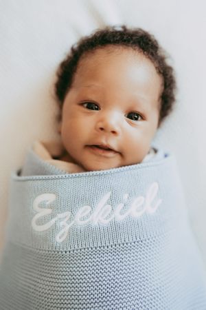 Baby swaddled in soft blue knit blanket with text embroidery showing adorable expressions.