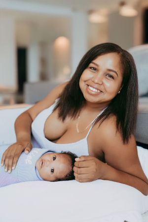 Intimate mother and baby portrait session on white bedding with soft natural lighting.