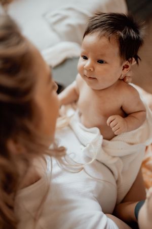 A smiling baby wrapped in white fabric gazes up with bright attentive eyes.