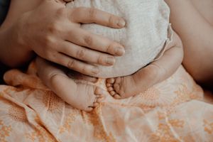 Close up of tiny baby feet and hands with gentle touch against peach colored fabric.