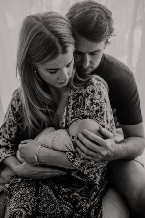 Intimate portrait of couple holding newborn baby in soft window light.