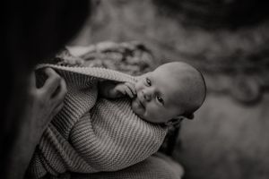 Black and white portrait of baby wrapped in knit blanket.