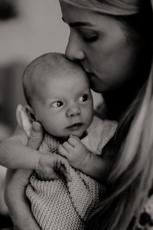 Black and white close-up of baby being kissed while looking to the side.