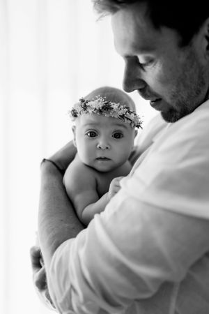 A tender black and white portrait of a baby wearing a delicate floral crown being held close.