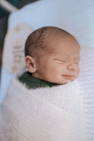Sleeping newborn baby wrapped in soft white blanket captured in gentle natural light.