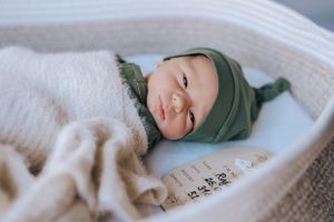 Infant wearing green outfit rests peacefully on white textured blanket.