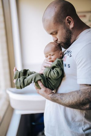 Parent in white shirt holding sleeping infant wearing olive green outfit.
