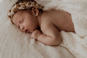 Sleeping newborn baby wrapped in soft white blankets on creamy textured backdrop.