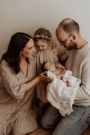 Family sharing intimate moments with newborn baby wearing white lace dress.