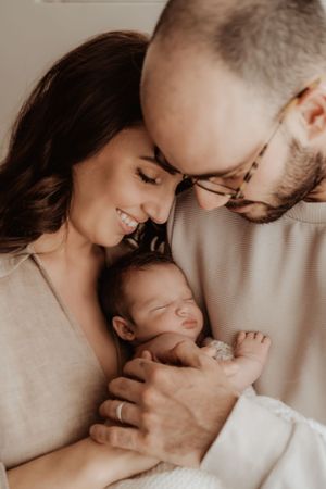 Parents embracing and bonding with their newborn in soft window light.
