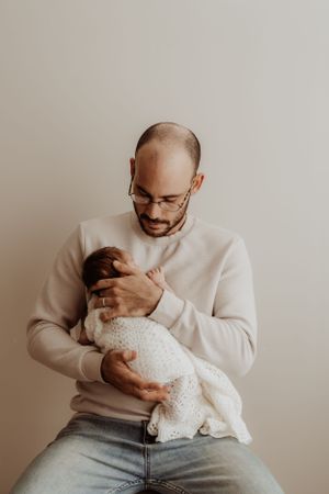 Parent in cream sweater holding sleeping newborn dressed in white lace.