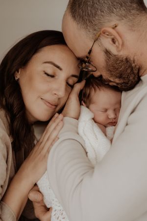 Tender family moment with newborn baby in white against neutral background.