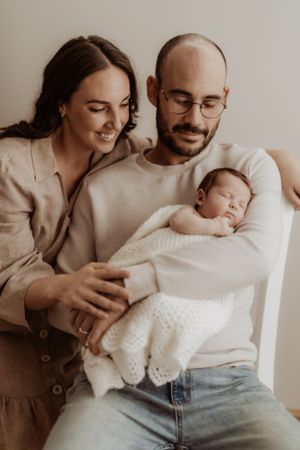 Loving parents cuddling with newborn baby in minimalist indoor setting.