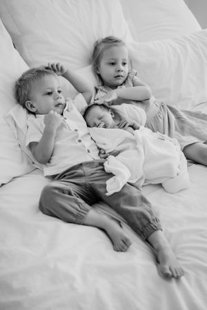 Black and white image of children relaxing together on white bedding.