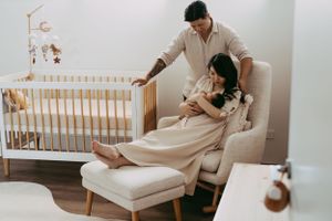 A couple relaxes together in a cozy nursery with a wooden crib visible in the background.