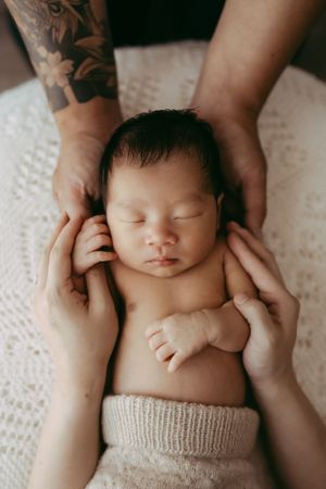 A peaceful sleeping newborn baby lies on white fabric while gentle hands cradle their head.