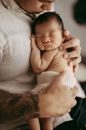 Gentle newborn portrait showing tiny sleeping baby being cradled against white clothing.