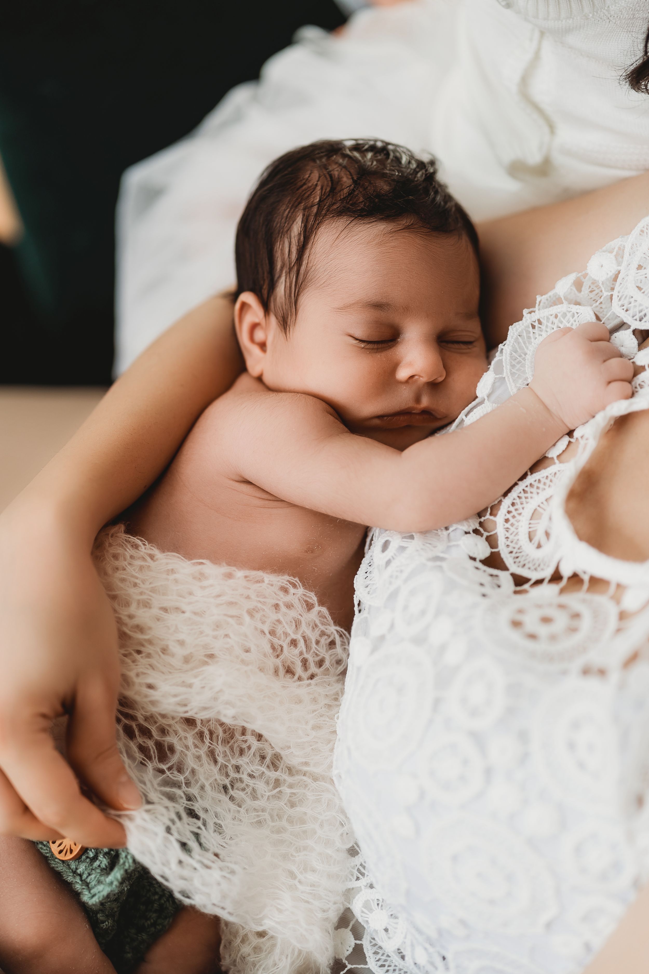 Sleeping newborn nestled against white lace fabric in an intimate close-up shot.