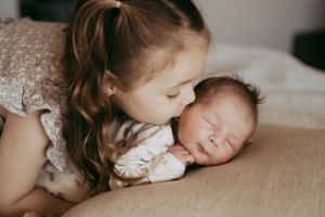 Siblings sharing gentle moment with newborn baby during indoor lifestyle photoshoot.