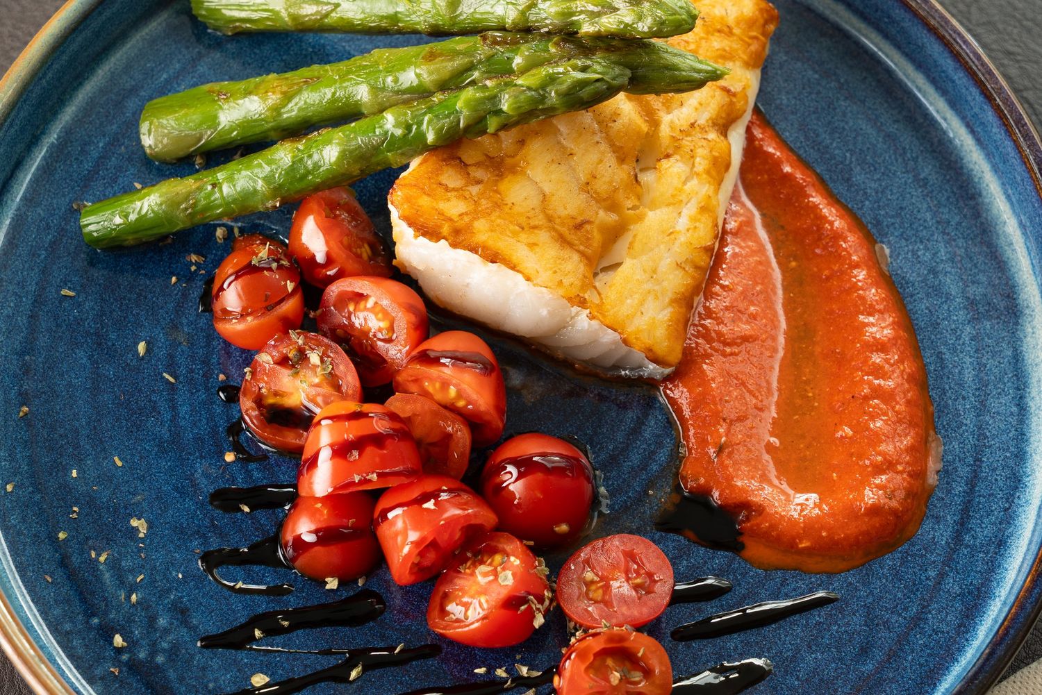 Grilled shrimp and asparagus served on a blue ceramic plate with drizzled balsamic glaze.