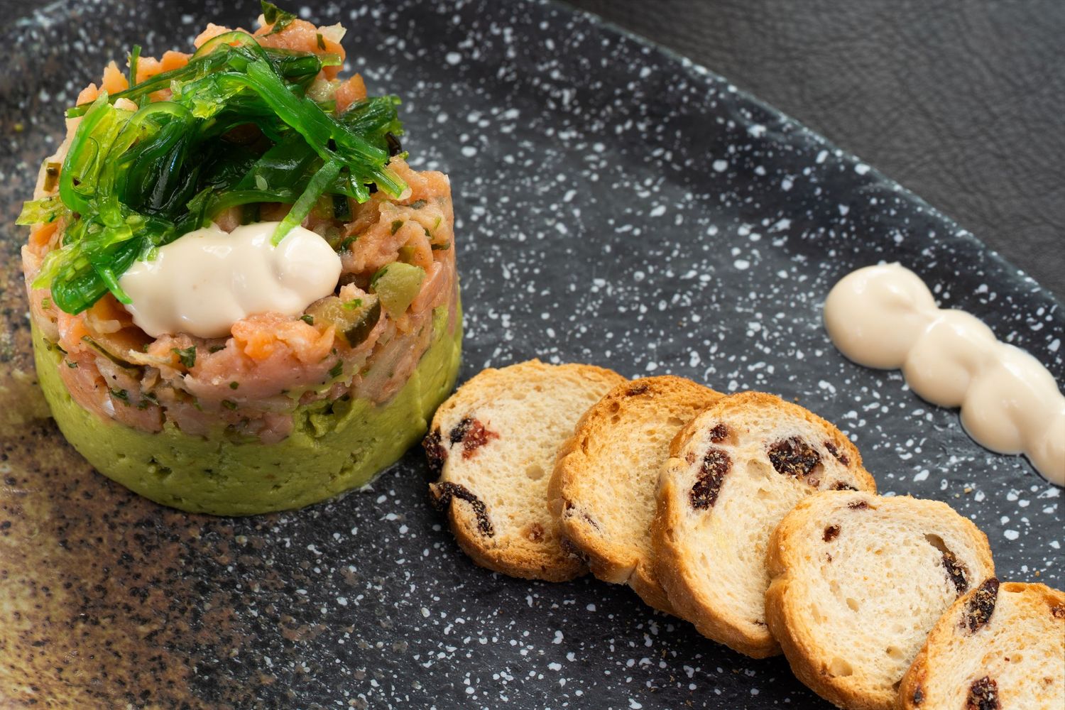 Elegant plated appetizer featuring tuna tartare with avocado and microgreens served with toasted crostini on dark slate.