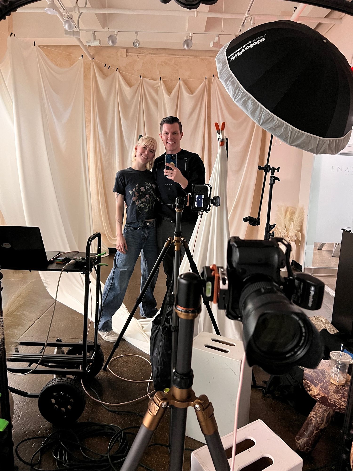 Two photographers pose together in a studio setting with professional lighting equipment.