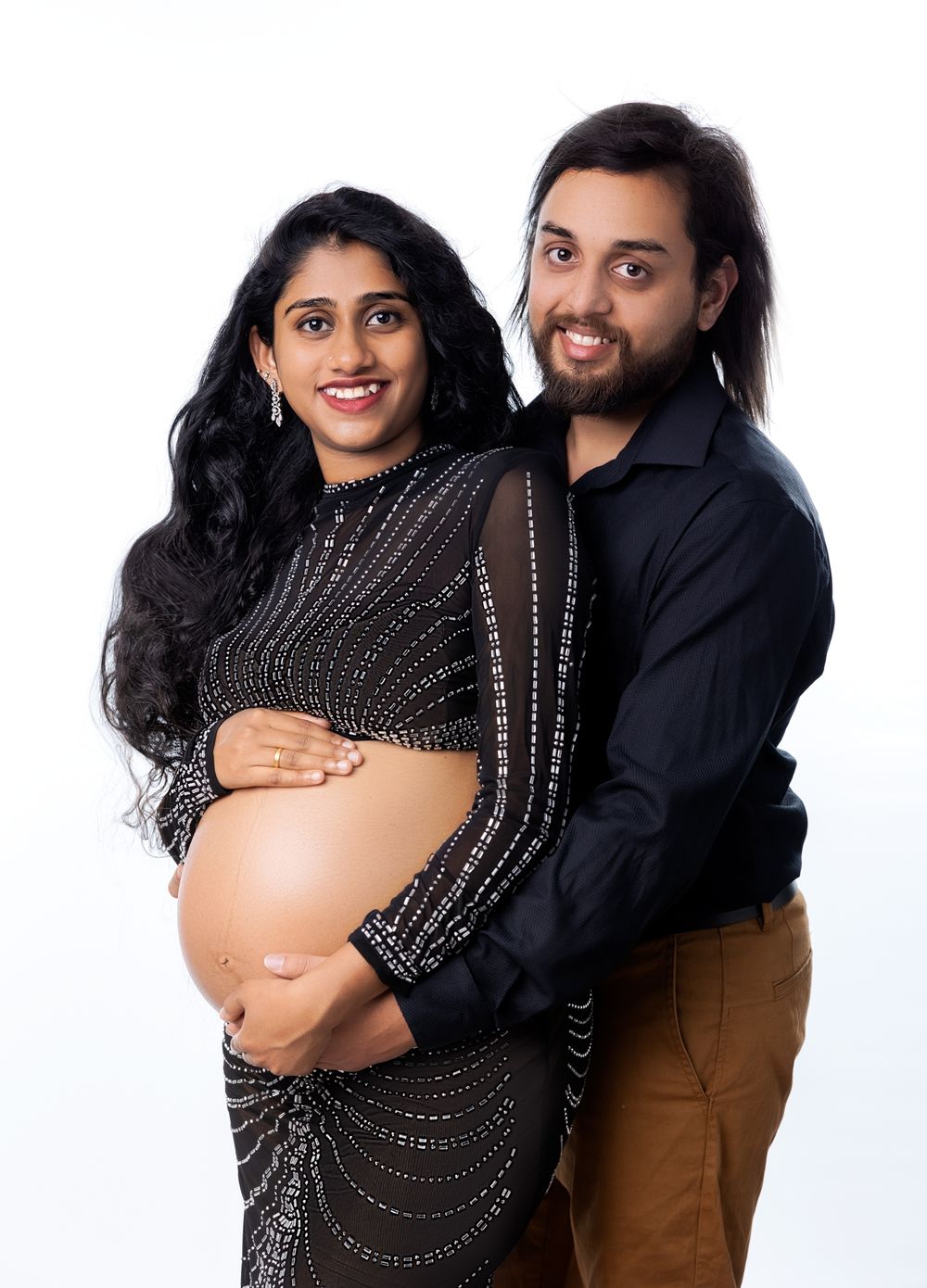 Maternity photo series showing couple in black and brown outfits against white backdrop with woman wearing sparkly dress.