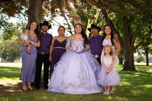 Group photo of quinceanera celebration with attendants in purple and lavender dresses under trees.