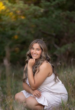 Portrait in white dress sitting in summer field during golden hour.