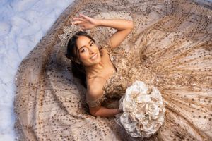 Aerial shot of person in glittery champagne-colored ball gown lying with white bouquet.